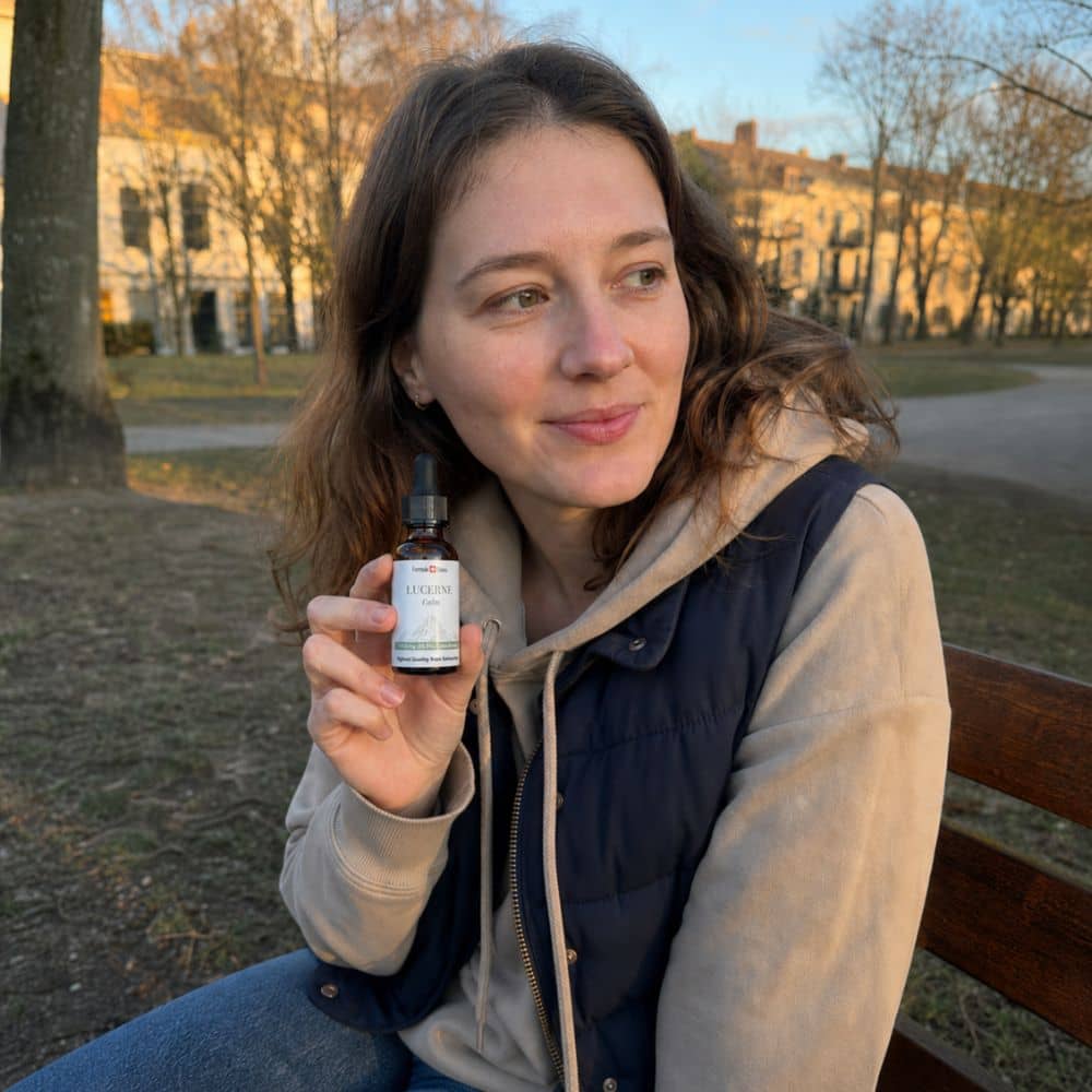 Nainen pitelee Lucerne-CBD-öljypulloa ulkona puistossa